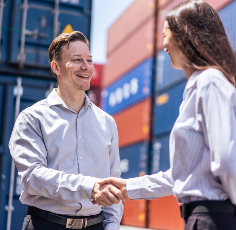 Caucasian businesswoman and businessman worker wor in container port. Attractive female and male making hand shake together after processes order at warehouse logistic terminal in cargo freight ship