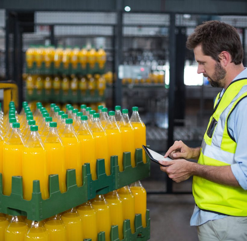 Factory worker maintaining record on juice bottles on digital tablet in factory